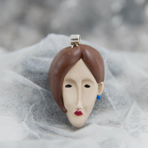Face form pendant of woman (inspired by Modigliani portraits) which is hand-sculpted from polymer clay and is on white see-through background